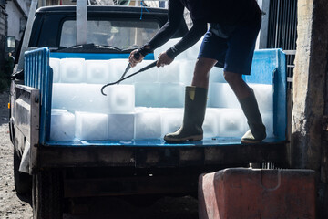 Man unloads ice blocks from a car with big iron hooks in fish market