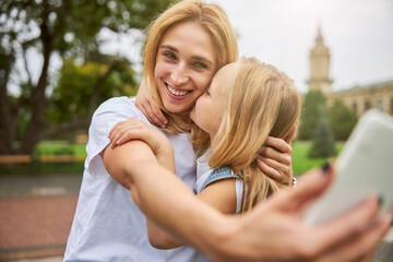 Fototapeta premium Smiling mother with female child doing selfie on the mobile