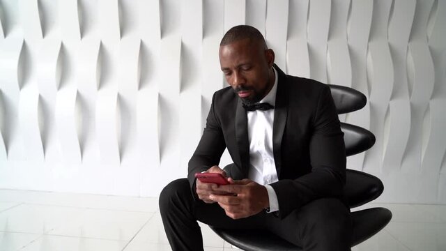 african man dressed in tuxedo with bow tie is calling by mobile and waiting