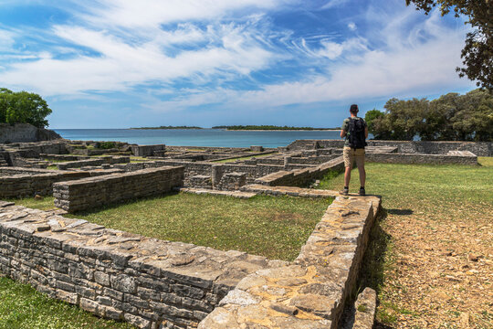 A tourist with a backpack standing of the top of roman ruins enjoying the view on the Adriatic sea at Brijuni national park, in Croatia.
