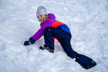 Fototapeta na wymiar Outdoor winter portrait of little cute girl wearing ski clothes. Girl climbing a snow slide.