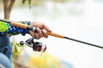 Fishing reel and rod in fisherman hand in a pond