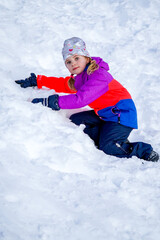 Fototapeta na wymiar Outdoor winter portrait of little cute girl wearing ski clothes. Girl climbing a snow slide.