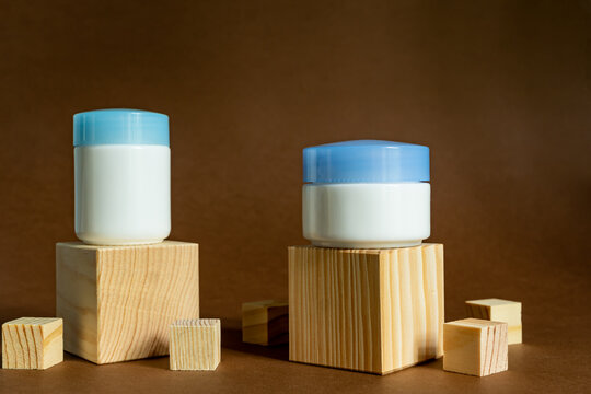 Display wooden podium with crem jars on a brown background. Face care containers. Cosmetics mockup. Day and night products
