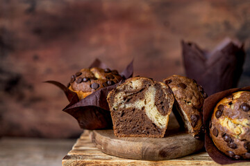 Soft and moist chocolate banana muffins with dark chocolate drops in wooden box, rustic table. Homemade baked twisted cupcakes. Natural light, selective focus, copy space