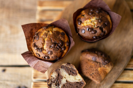 Soft and moist chocolate banana muffins with dark chocolate drops in wooden box, rustic table. Homemade baked twisted cupcakes. Natural light, selective focus, copy space