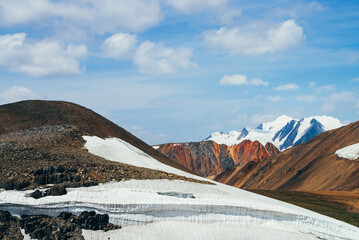 Wonderful view to small glacier on stony hill under blue sky with clouds. Beautiful alpine landscape with ice cornice on rock. Colorful mountain scenery on high altitude. Majestic highland nature.