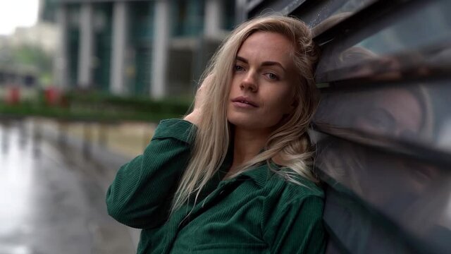beautiful blonde woman is seducing camera on street, portrait in rainy day