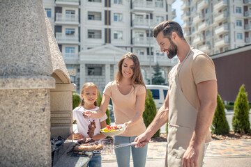 Dad grilling meat while his daughter and wife standing next to him