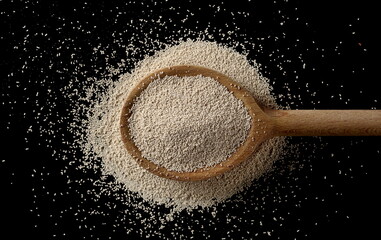 Active dry yeast granules pile with wooden spoon isolated on black background and texture, top view...