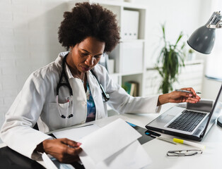 Woman doctor with stethoscope looking at medical papers at her office working hard