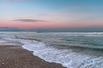 Sea with waves, sea foam and sandy beach at dusk