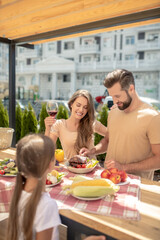Young cute family having dinner outside and looking amused
