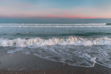 Sea with waves, sea foam and sandy beach at dusk