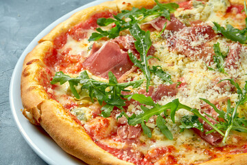 Homemade pizza with jamon, arugula and parmesan in a white plate on a concrete background