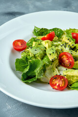 Vegetarian salad with avocado, lettuce and cherry tomatoes in a white plate on a concrete background
