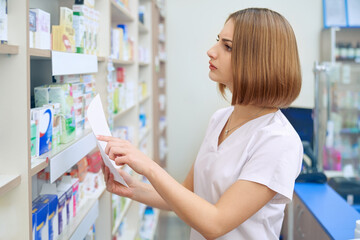 Female pharmacist searching for medicaments from prescription.