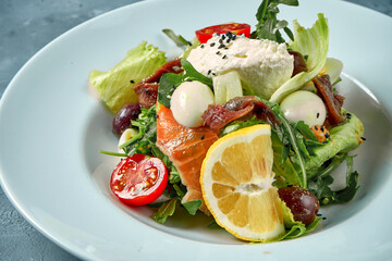 Appetizing salad with tomatoes, salmon, anchovies and cream cheese in a white plate. Concrete background