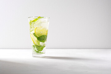 A mojito cocktail stands in a tall glass with ice on a gray concrete background.