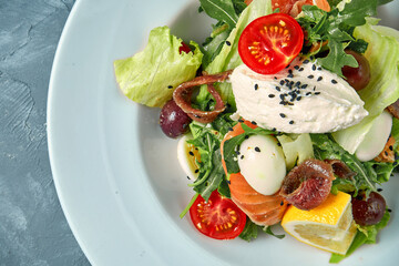 Appetizing salad with tomatoes, salmon, anchovies and cream cheese in a white plate. Concrete background