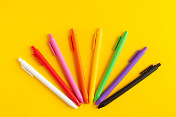 Multi-colored pens on a yellow background. The concept of the beginning of the school year, office and school supplies.