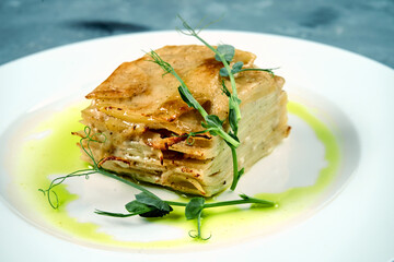 Baked potato gratin with cream and cheese in a white plate on a concrete background