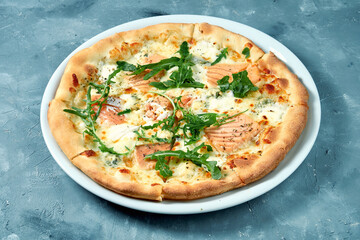 Appetizing cheese pizza with salmon and arugula in a white plate on a gray background. Top view. Seafood pizza