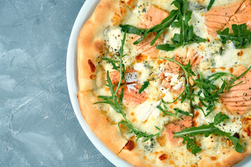 Appetizing cheese pizza with salmon and arugula in a white plate on a gray background. Top view. Seafood pizza