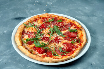Italian pizza with salami, arugula and parmesan on a white plate. Concrete background. Top view