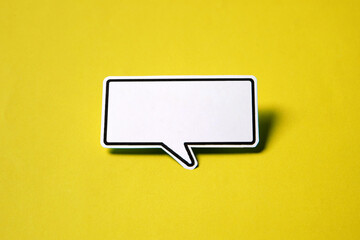 Blank speech bubble on white paper isolated on yellow paper background with drop shadow.
