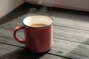 Close up of pink coffee cup on table in sunlight against window on black wooden table