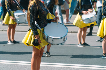 Street performance of festive march of drummers girls in yellow black costumes on city street....