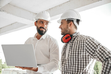 Positive male engineers with laptop at construction site