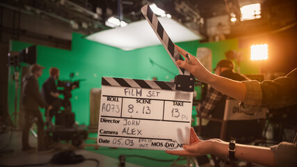 On Film Studio Set Camera Assistant Holds Clapperboard. Green Screen Scene with Talented Cameraman in the Background. Close-up Shot. - obrazy, fototapety, plakaty