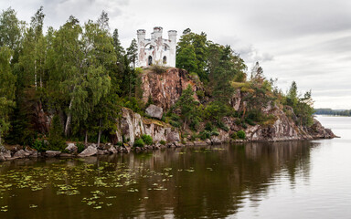 Fototapeta na wymiar Autumn Monrepos Park with small vintage castle on granite rock near big lake