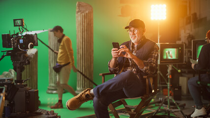 Prominent Successful Director Sitting in a Chair on a Break Using Smartphone. On the Studio Film...