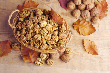 Walnuts in a wicker basket and walnuts in shells on a wooden table.