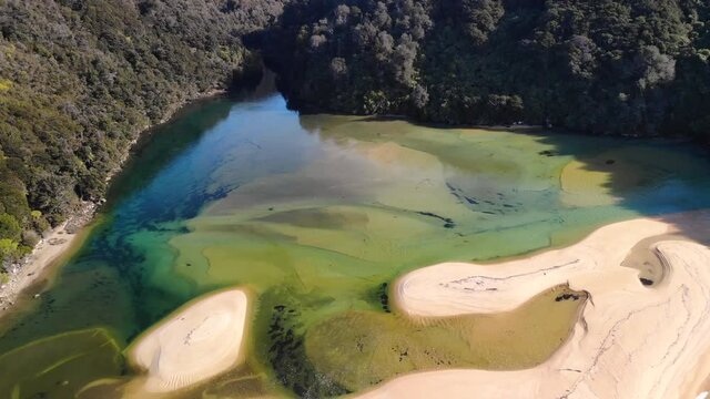 Small beautiful sandy beach across the sea aerial, birds eye view of jungle forrest Abel Tasman, New Zealand. Warm day full of colours in paradise.