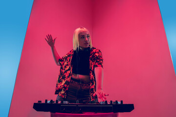 Mood. Young female stylish, fashionable musician performing on blue-red background in neon light. Concept of music, hobby, festival, entertainment, emotions. Joyful party host, DJ, portrait of artist.
