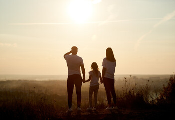 Silhouette of a family - father, mother and daughter standing on the hill with their backs to the...