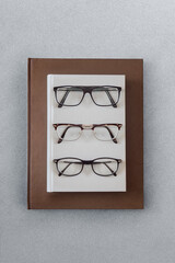 Three different types of glasses on the hardcover of a gray book that is resting on a large brown leather copy on top of an elegant gray textured table. Education and reading concept.