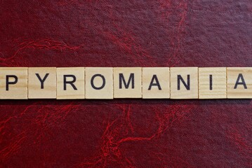 text the word pyromania from gray wooden small letters with black font on an red table