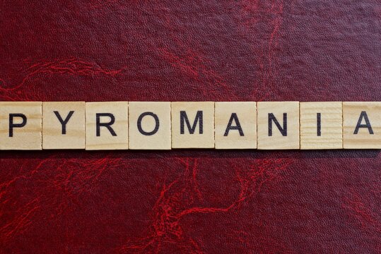 text the word pyromania from gray wooden small letters with black font on an red table