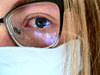 Nahaufnahme Makro eines Auges versteckt hinter schwarzer Brille, hellblauer Maske und blonden...