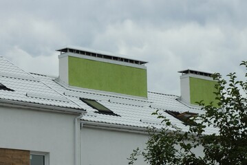 white tiled roof with windows on a large house and two green concrete chimneys against a gray sky