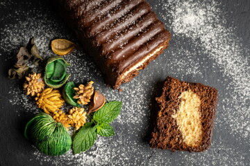 Chocolate cake on black background, icing sugar and decorative herbs