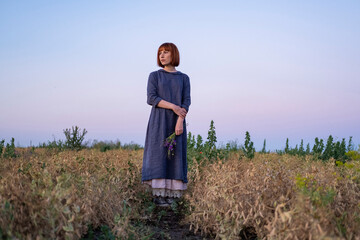 Young redhead woman with  
freckles in vintage handmade dress walk in fields with flowers 