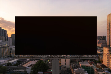 Blank black road billboard with Bangkok cityscape background at sunset. Street advertising poster, mock up, 3D rendering. Front view. The concept of marketing communication to promote or sell idea.