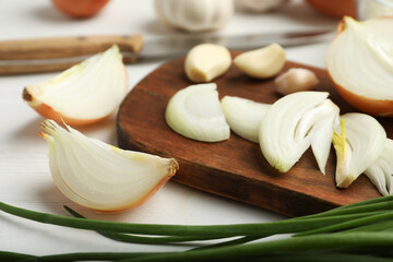 Board with cut onion and garlic on white wooden table