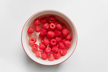 Top view above closeup bowl of fresh raspberries soaking in a water with isolated white grey background